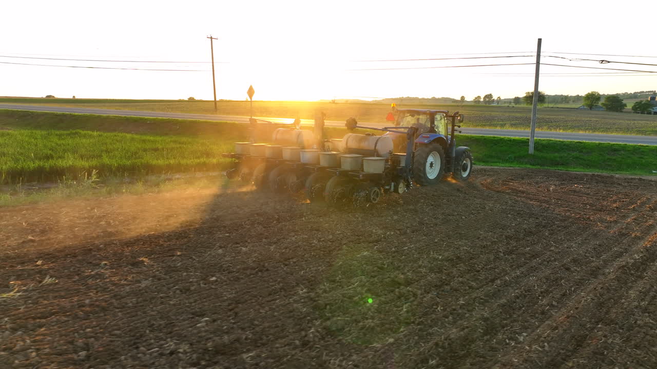 Low drone shot directly behind planter. Rotate out of dust to see beautiful sunset. New Holland tractor pulls large planter. American farming theme