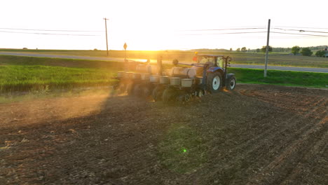 low drone shot directly behind planter. rotate out of dust to see beautiful sunset. new holland tractor pulls large planter. american farming theme