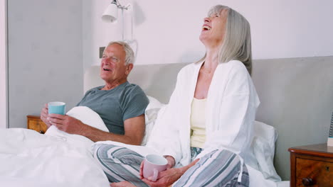 Retired-Couple-Wearing-Pajamas-Sitting-In-Bed-Drinking-Tea