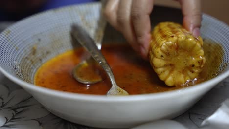 corn cob being dipped in spice sauce inside bowl