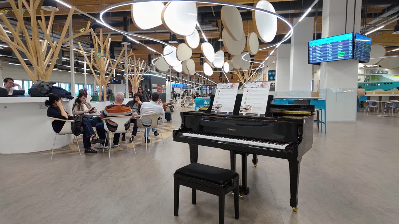 The new modern, bright and spacious terminal of Liszt Ferenc Airport with waiting passengers and a piano in Budapest, Hungary.