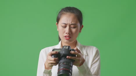 primer plano de fotógrafo asiático mirando las imágenes en la cámara luego teniendo dolor de cabeza mientras estaba de pie en el fondo de la pantalla verde en el estudio