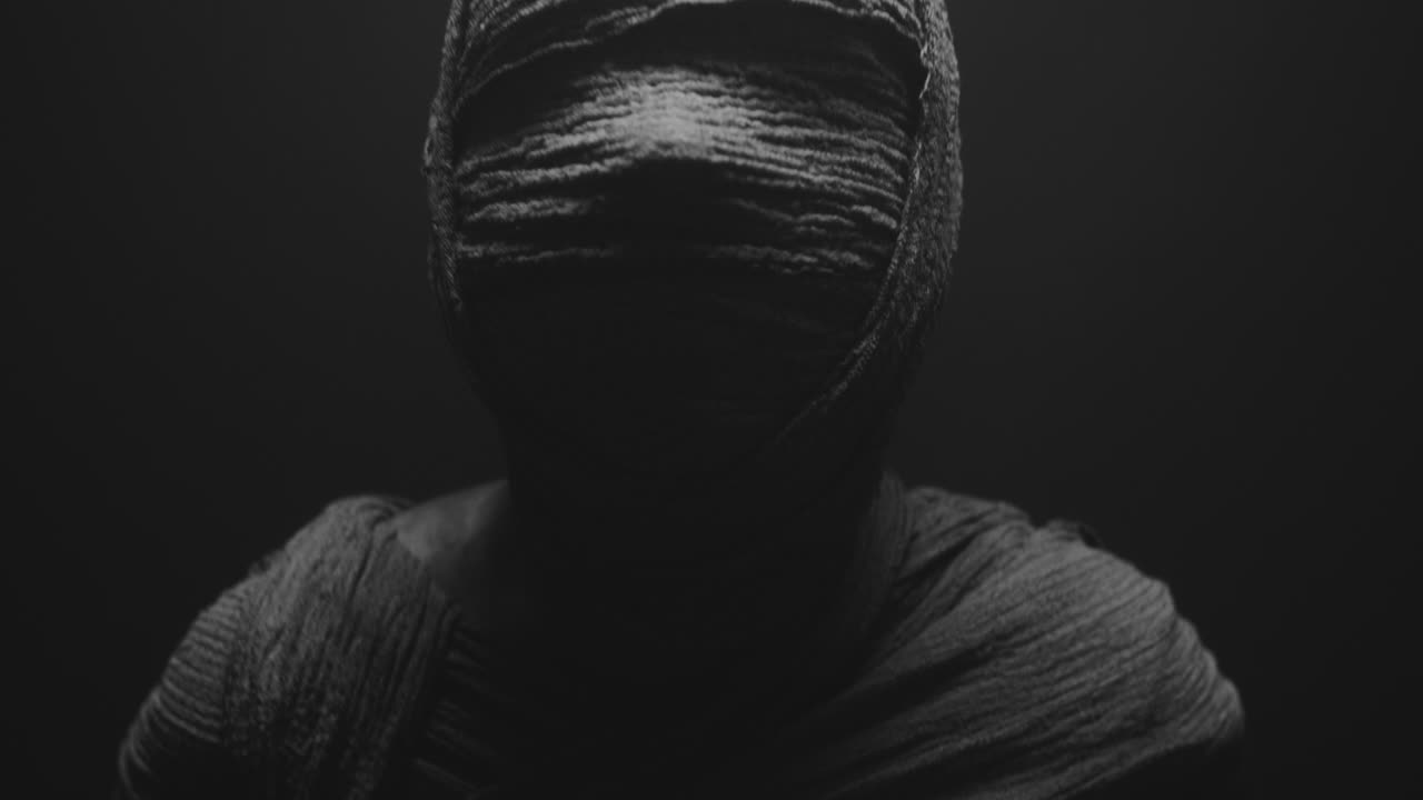 Una donna mummificata su uno sfondo scuro alza e poi gira la testa.