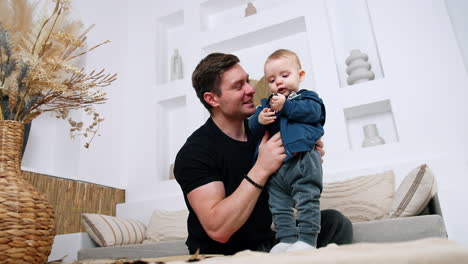 father holds the standing little infant boy focused on the bracelet in his hands. dad taking care of his son. low angle view.