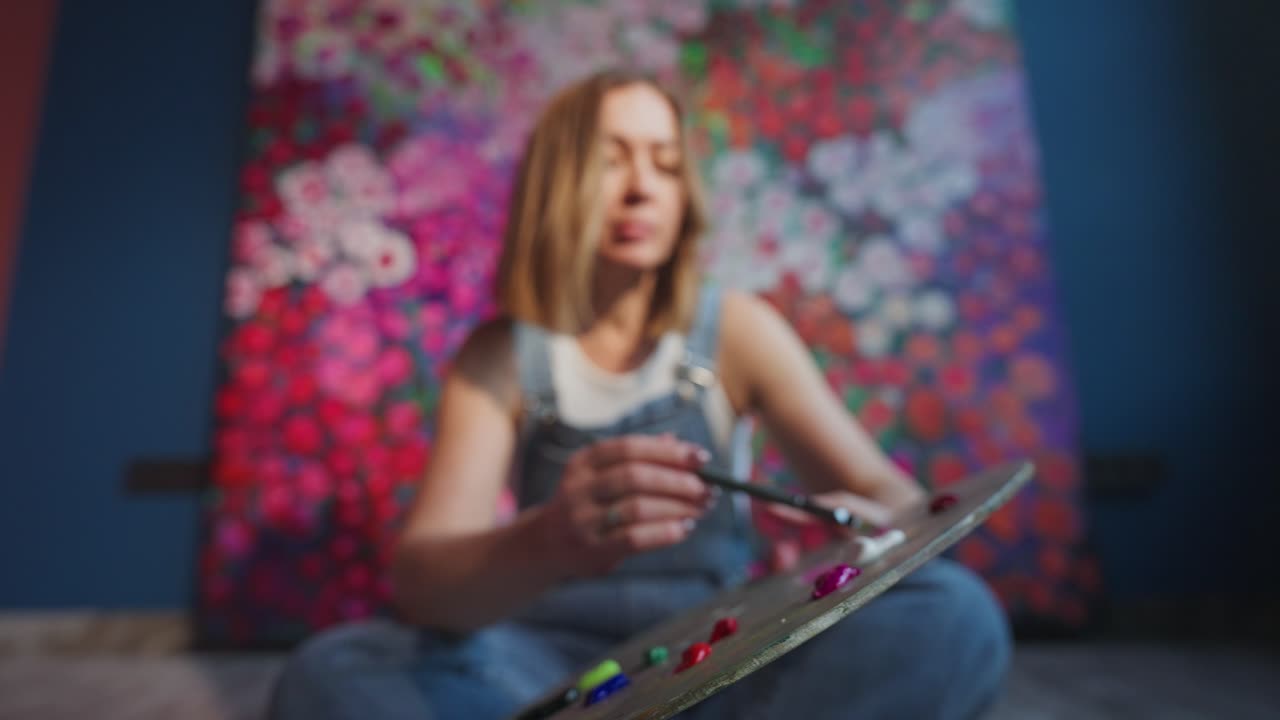 筆で絵の具パレットの色を混ぜる女性画家