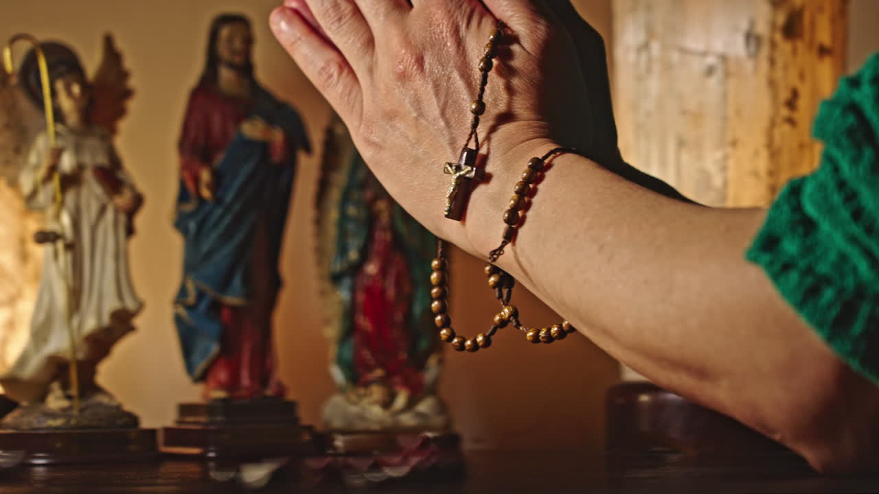Primo piano di mani in preghiera che tengono un rosario con statue religiose