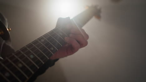 close-up of a guitarist's hands playing a red guitar, highlighted by a focused light beam in a dimly lit room as the camera zooms in