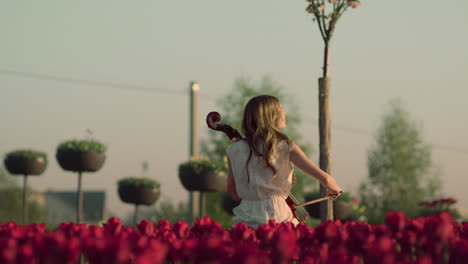 back view of unrecognizable woman with cello sitting in spring garden outdoors.