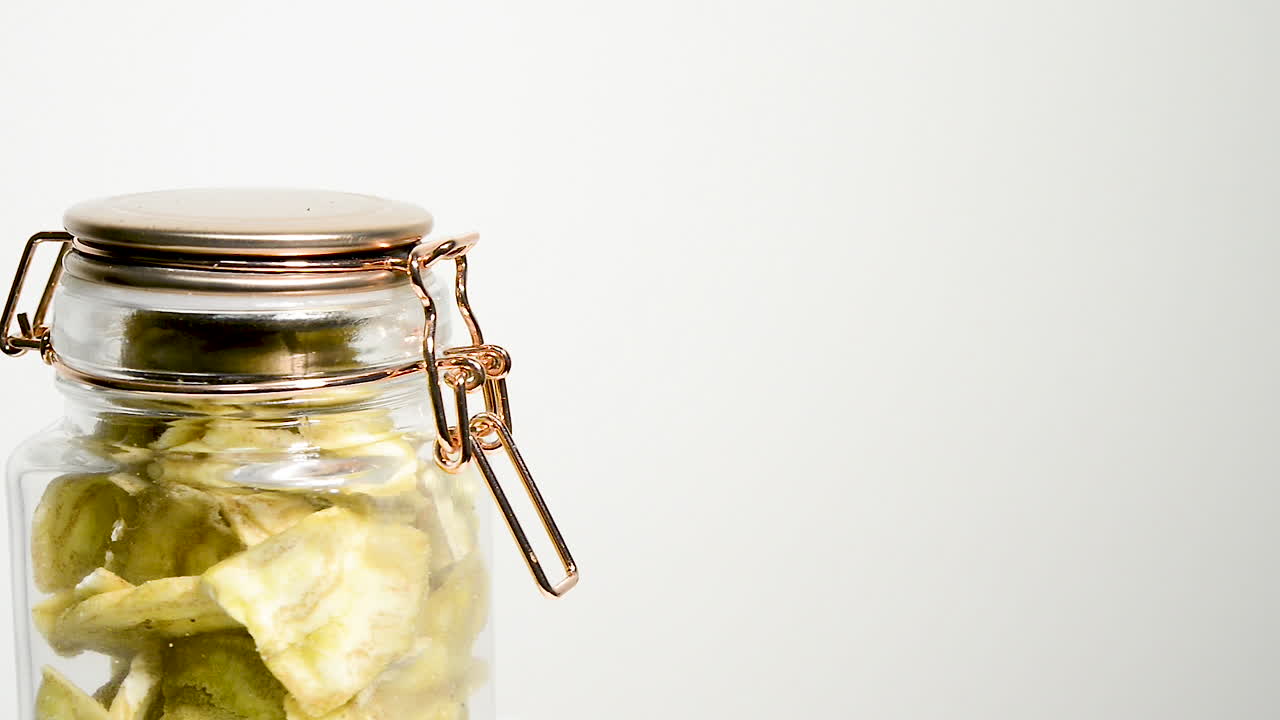 un frasco de chips de plátano secos girando lentamente, aislado en un fondo blanco