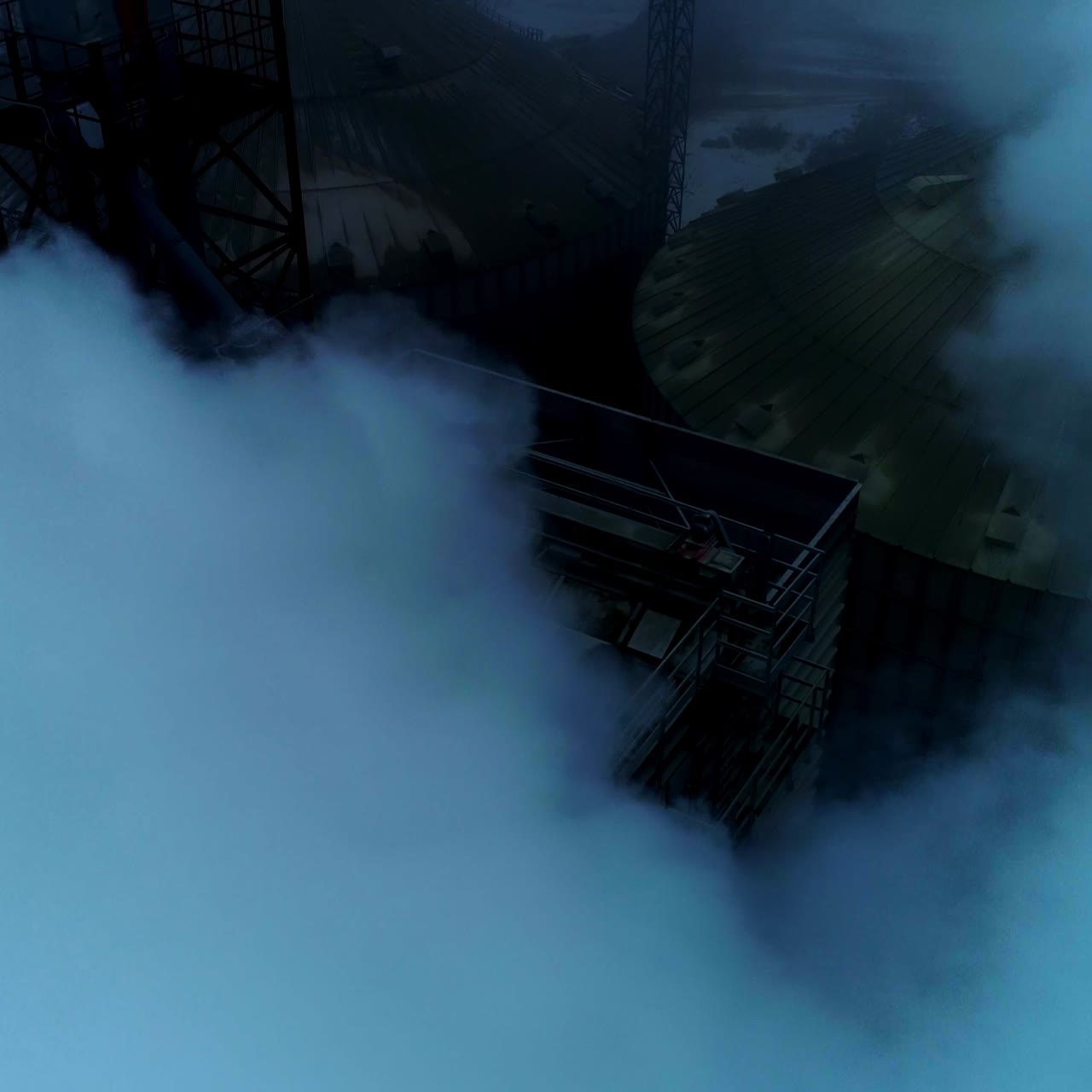Five thick pipes letting out heavy white smoke as a result of grain processing. Rising over the big agricultural plant at foggy weather day