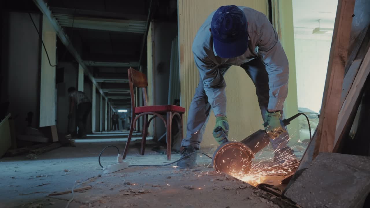 Reparationsarbete i huset. En man skär metall och betong med en metallsåg. Översyn av huset och restaurering av korridoren.