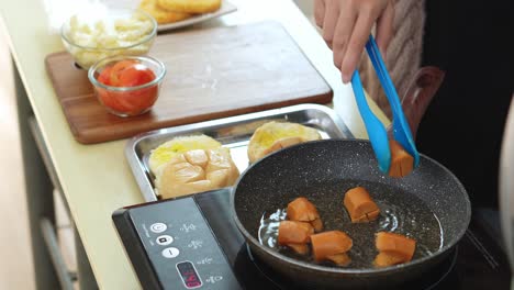 young woman frying sausages with tongs on hot pan