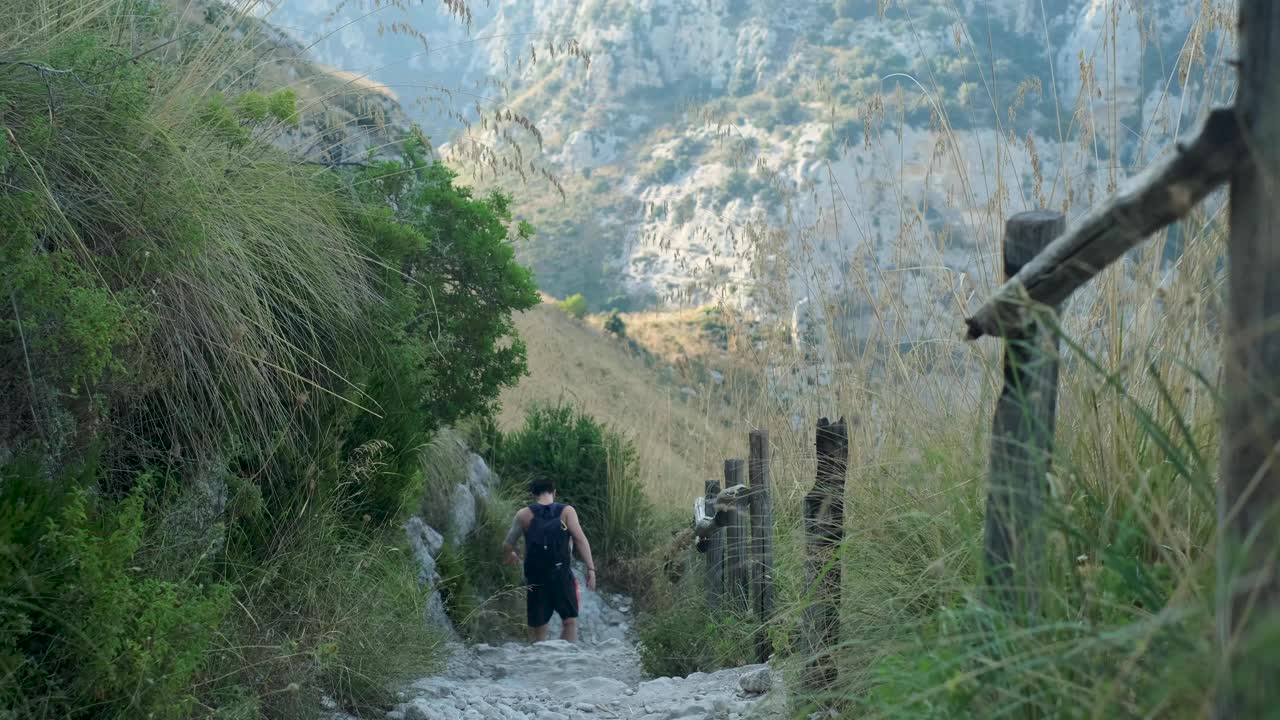 Slow Motion Downward Tracking Wide Shot of Young Asian Adult Male Walking Down Dry Stony Path in Beautiful Mountain Valley