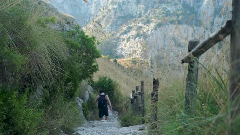 slow motion downward tracking wide shot of young asian adult male walking down dry stony path in beautiful mountain valley