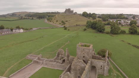 Aerial-fly-over-of-13th-century-Abbey-ruins-with-foot-trails-leading-to-historic-"Rock-of-Cashel"-in-the-background,Tipperary-Ireland