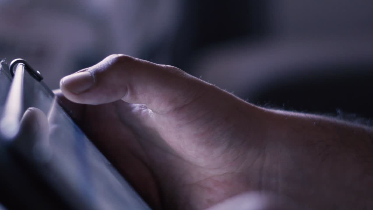 Shooted in slow motion showing man's hands browsing social media or playing with a mobile tablet at evening (dark space)