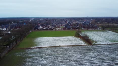 Vista-Aérea-Sobre-La-Tradicional-Ciudad-Holandesa-Rodeada-De-Campos-Agrícolas-Cubiertos-De-Nieve-Derretida