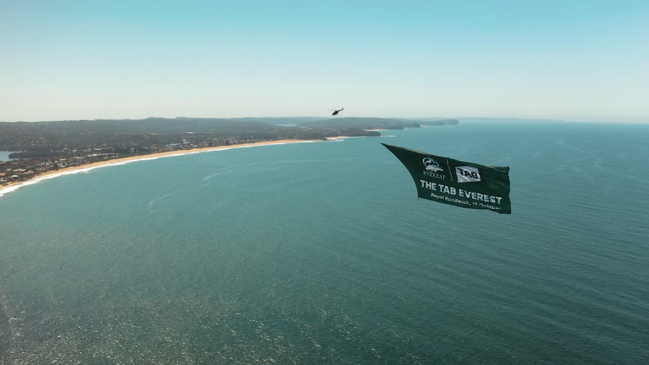 Helicopter aircraft flying up the coast of Sydney Australia towing a banner along Northern Beaches above the ocean