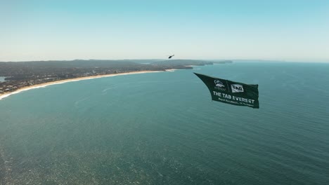 helicopter aircraft flying up the coast of sydney australia towing a banner along northern beaches above the ocean