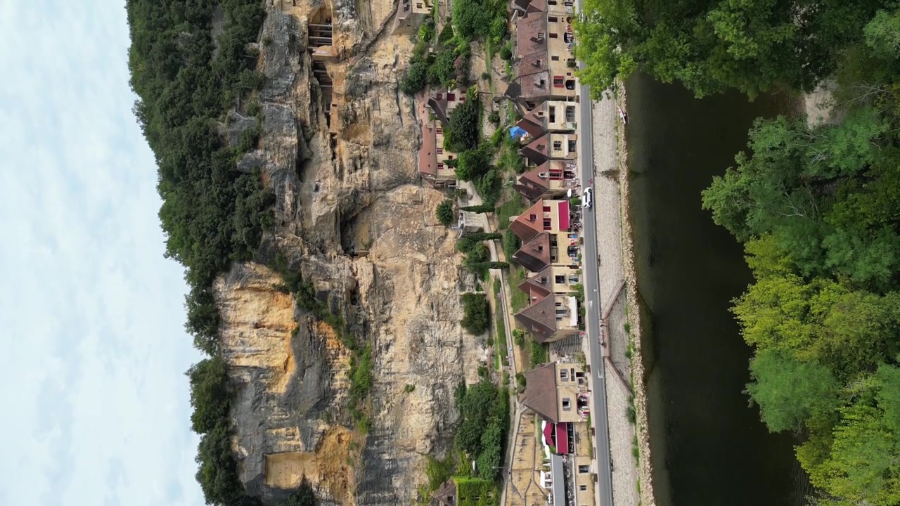 Vista aérea con dron en la campiña francesa de una pequeña ciudad medieval antigua debajo de un acantilado de piedra, rodeada por un bosque verde y un río que la rodea en La Roque Gageac, vista vertical