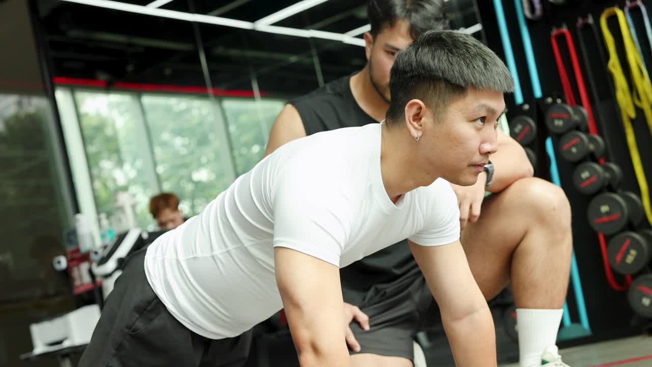 A trainer assists a client with a plank exercise in a well-lit gym, focusing on form and technique