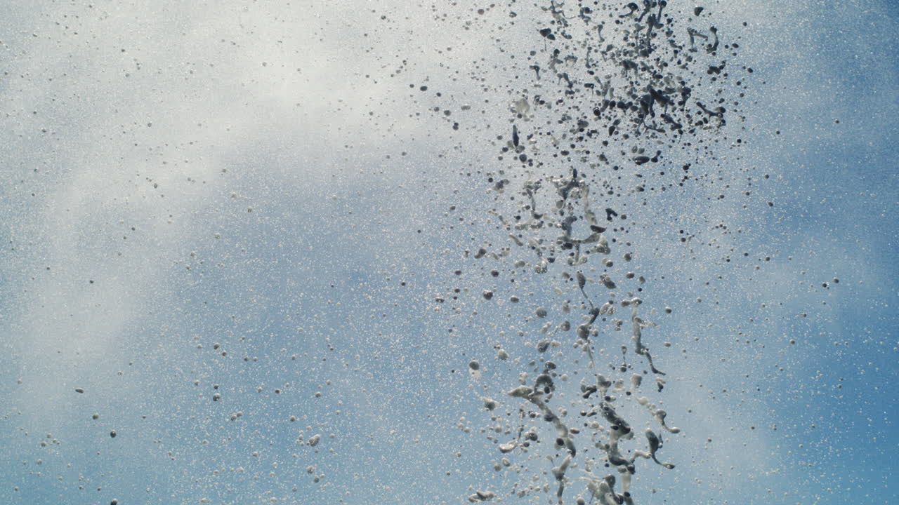 Super slow motion burst of ocean spray shooting upward into bright daylight sky