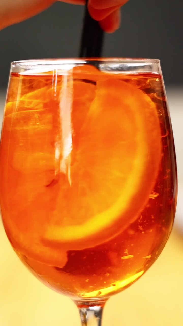 Mão mexendo um coquetel Aperol Spritz com rodelas de laranja