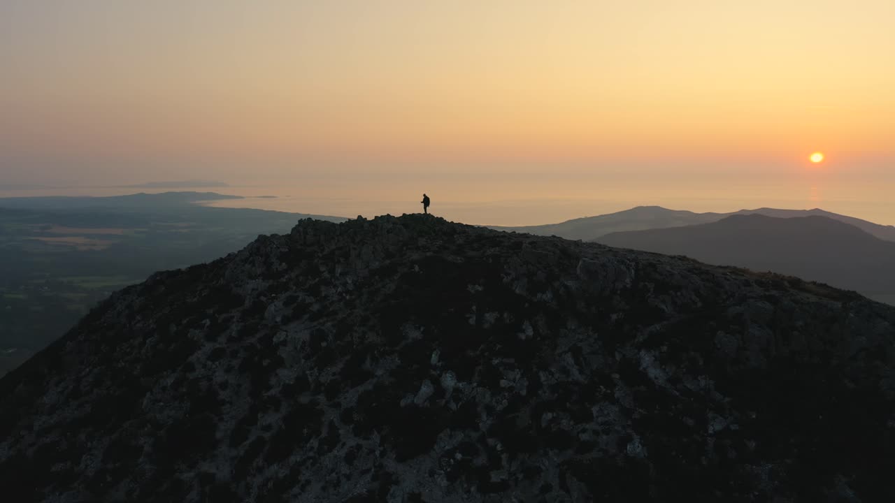 Ripresa aerea - Sorvolando l'uomo da davanti a dietro, in piedi sulla cima della montagna, che ammira uno splendido tramonto o alba sulle vette.
