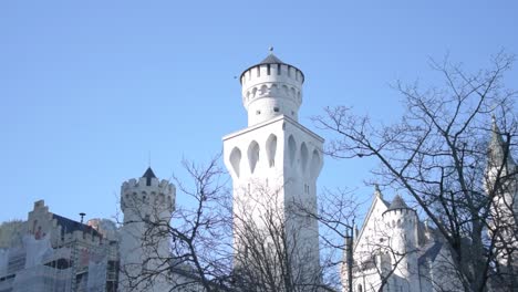 revealing the snow covered mountains behind the neuschwanstein castle towers under a cloudless, cold blue sky