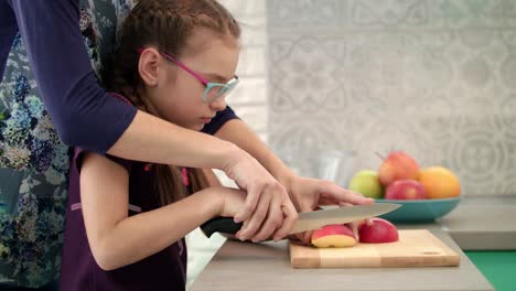 La-Mujer-Ayuda-Al-Niño-A-Cortar-Una-Rodaja-De-Manzana.-Madre-E-Hija-Cocinando-Juntas