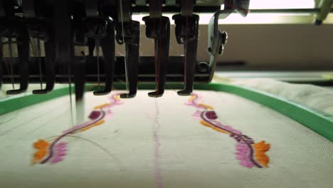 máquina de bordar moderna que cose un intrincado diseño floral en naranja, rosa y negro