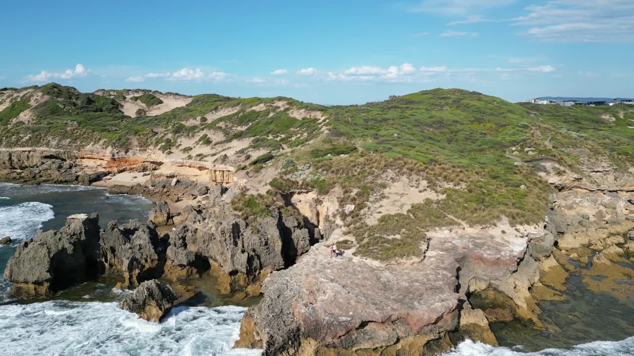 Rocky sea cliffs with big ocean waves crashing on the shore, wide aerial orbit view