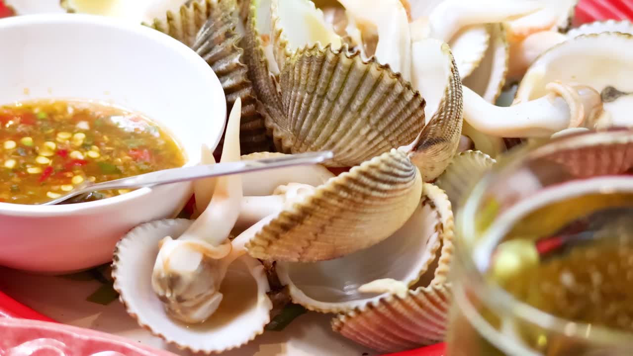 Close-up of clams with spicy dipping sauce and a refreshing beverage on a vibrant table setting.
