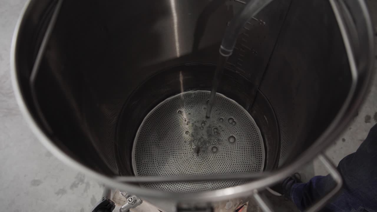 agua que se vierte de una manguera de plástico y se llena dentro de una olla o tetera de metal grande, ángulo alto de cerca