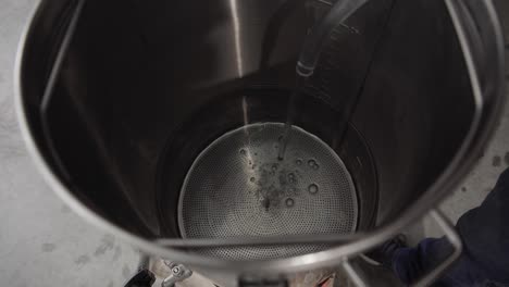 water pouring from a plastic hose and filling inside of a large metal pot or kettle, high angle close up