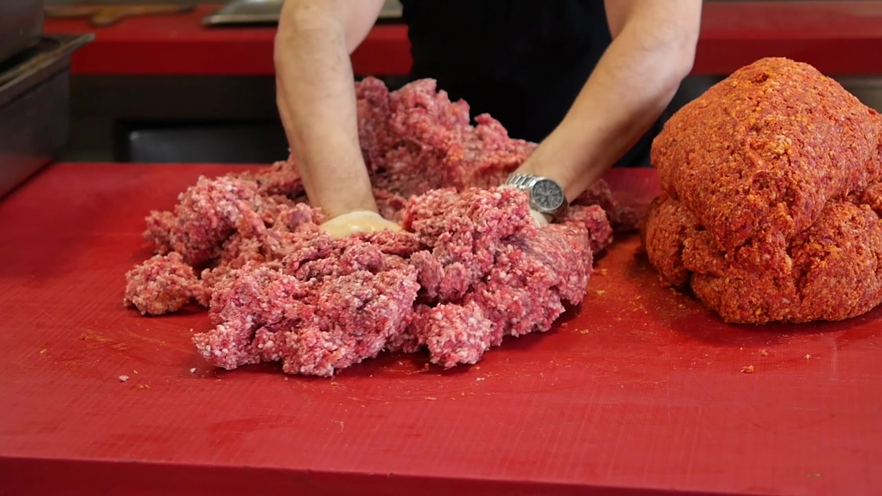 Koch knetet Hackfleisch auf roter Arbeitsplatte