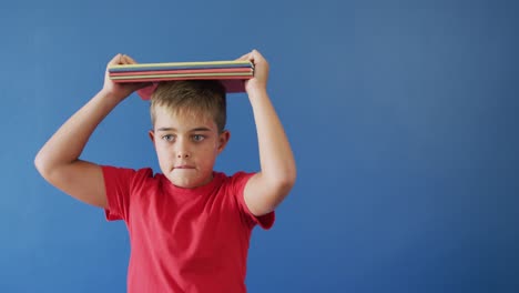 retrato de un niño caucásico feliz sosteniendo libros en la cabeza sobre un fondo azul, espacio de copia, cámara lenta