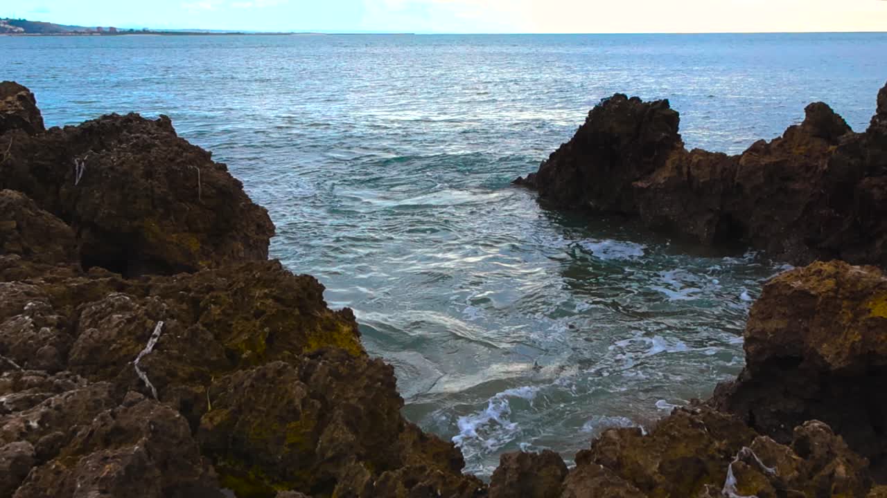 Veduta in una giornata nuvolosa dell'acqua oceanica blu-verde che si riversa impetuosamente attraverso una stretta insenatura rocciosa lungo la costa portoghese.