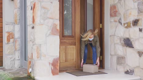 woman wearing face mask picking up the package left on the door