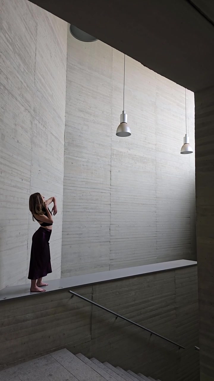 Una donna posa elegantemente in uno spazio architettonico minimalista ricco di design contemporaneo.