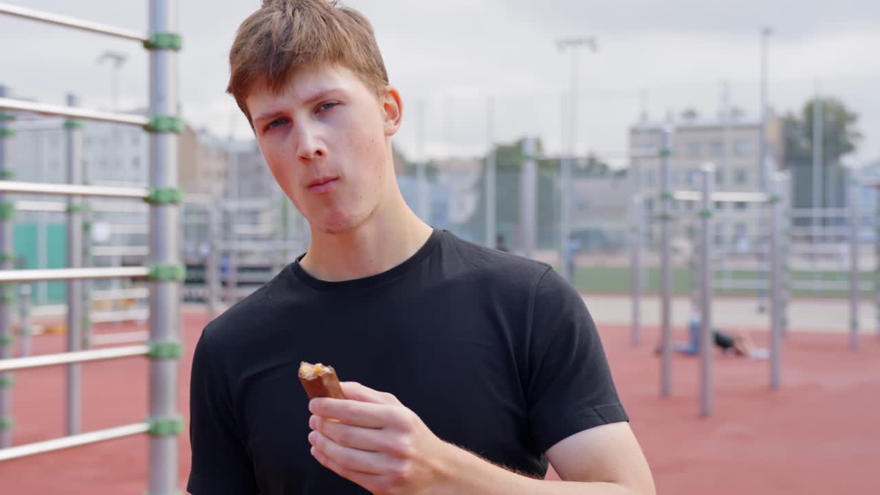 Athletic man chews protein snack while looking around, preparing mentally for training