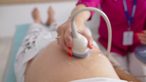 young pregnant woman getting ultrasound from female doctor in clinic. pregnancy and healthcare concept. prenatal screening.