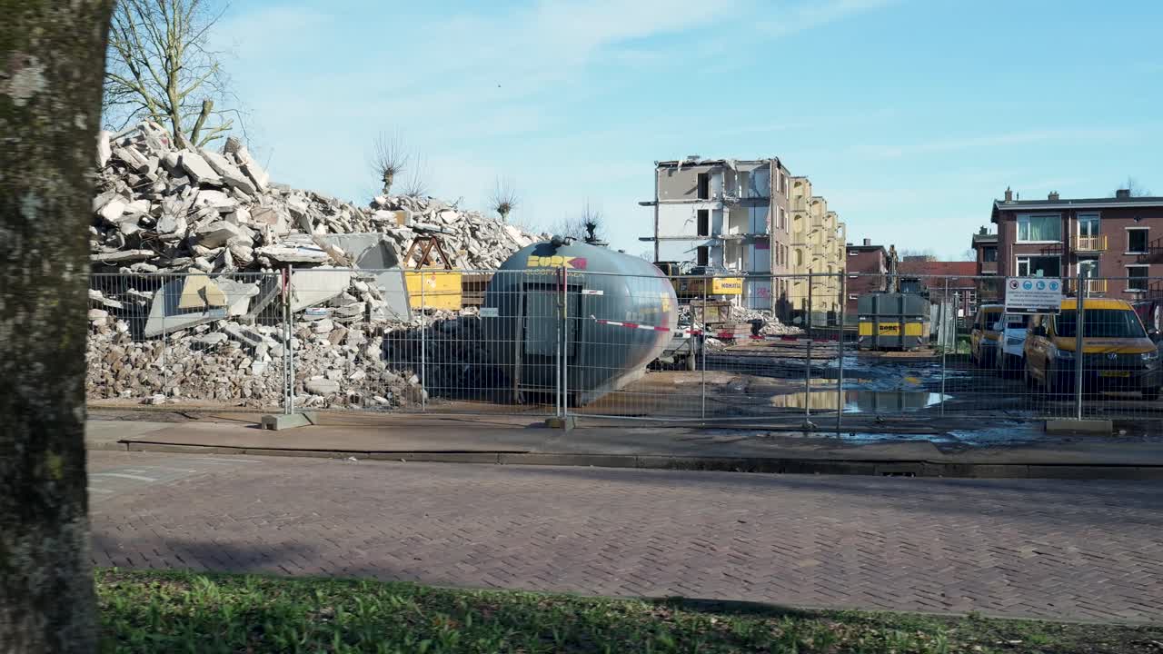 Pelleteuse sur un camion de transport passant devant un site de démolition avec des cyclistes