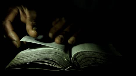 rezando a dios con la mano en el fondo negro de la biblia con la gente metrajes