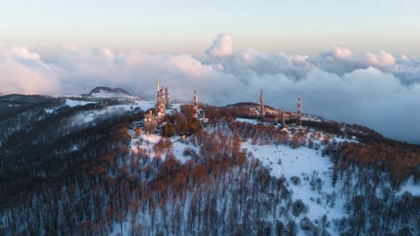 Radio station with masts on snowy mountain above clouds, timelapse.
