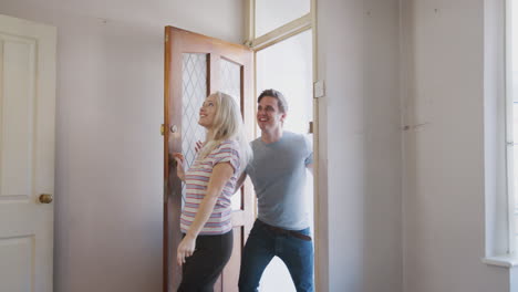 excited young couple opening front door of new home and hugging in empty room