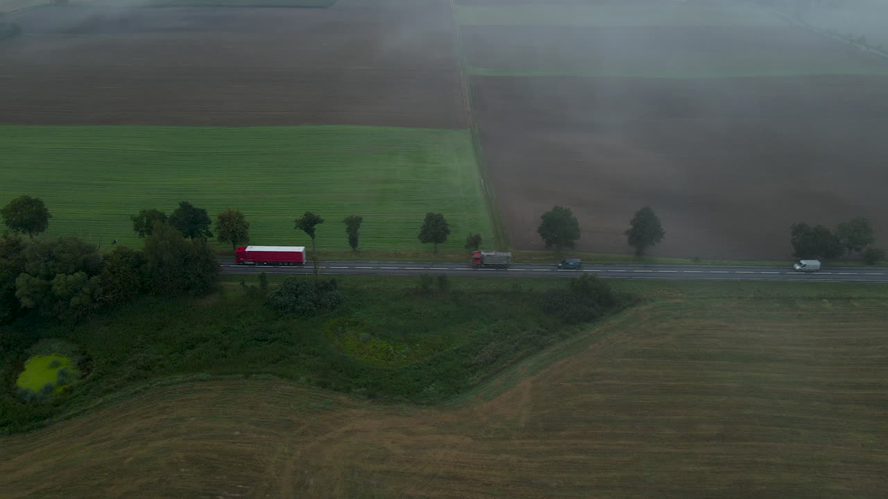 안개 속에서 농업 분야 사이의 시골 도로에서 운전하는 산업용 트럭과 자동차를 보여주는 항공 보기