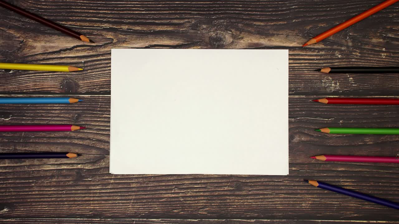 Colorful pencils around white paper on wooden background - Stop motion