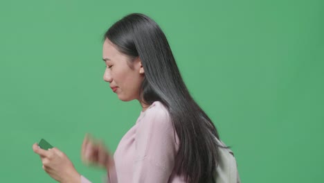 화가 난 아시아 여성 학생이 모바일 게임을 하고 녹색 스크린 스튜디오에서 는 동안 패배합니다.