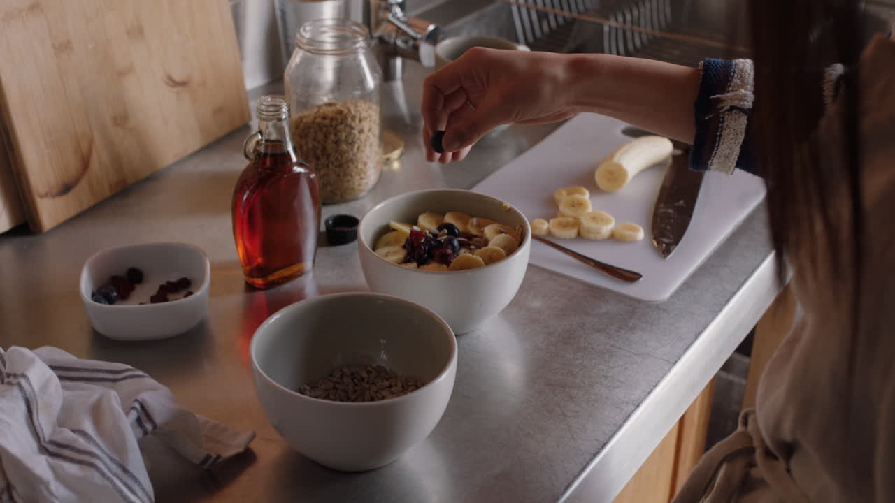 joven asiática desayunando en la cocina disfrutando de cereales de avena saludables mezclados con fruta relajándose en casa el fin de semana